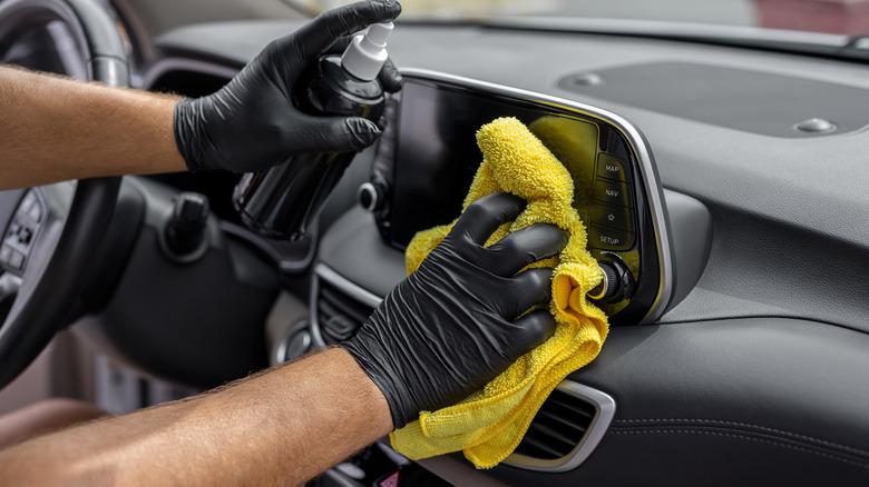 a man with black gloves spraying and cleaning the inside of a car with a yellow rag