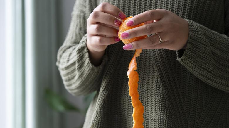 person taking the peel off an orange by hand