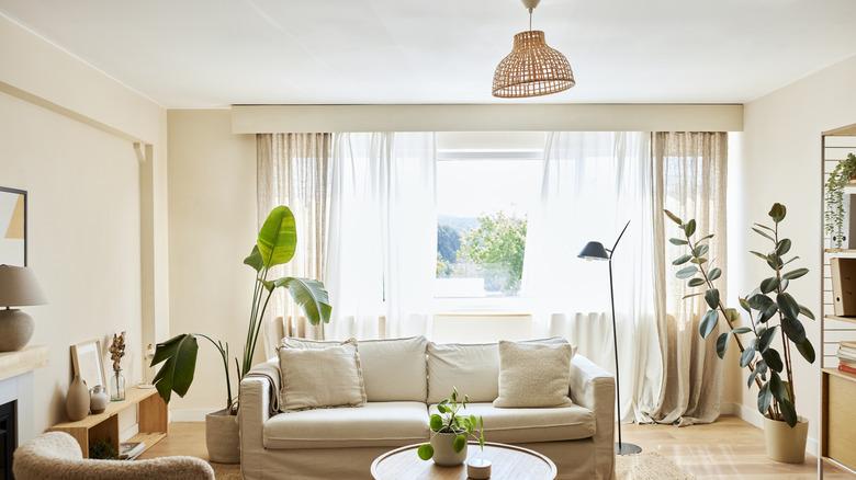 A living room with neutral colored furniture and cream colored, textured curtains hanging over the window.