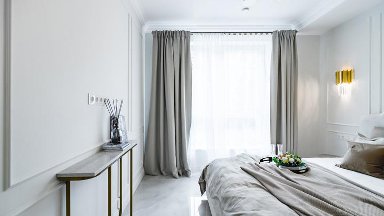 A bedroom with framed out wainscoting, white walls, and gray accents, including gray curtains.