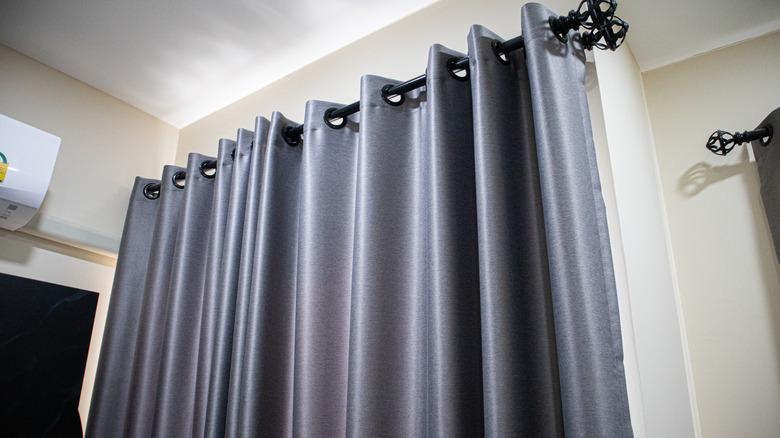 A metallic blue, silk curtain hung on a shiny black, statement, curtain rod.