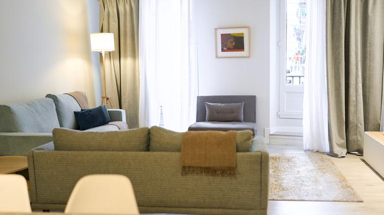 A living room with two sofas and an armchair, with khaki and white curtains in the background.
