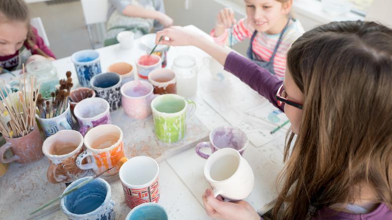 Kids painting at craft table with brushes and coffee mugs