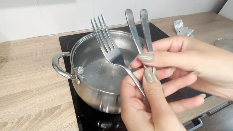 Cutlerty held in front of pot with water and aluminum foil
