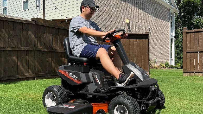 man riding on lawn mower on lawn with fence in the background