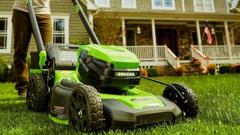 close up of man pushing lawn mower in back of house