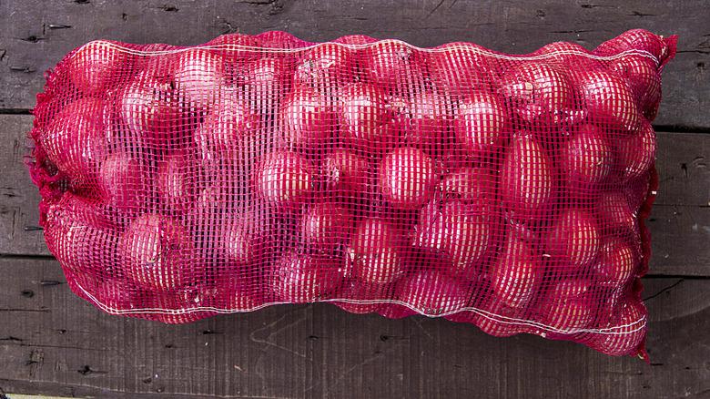 Mesh bag of onions on wood table