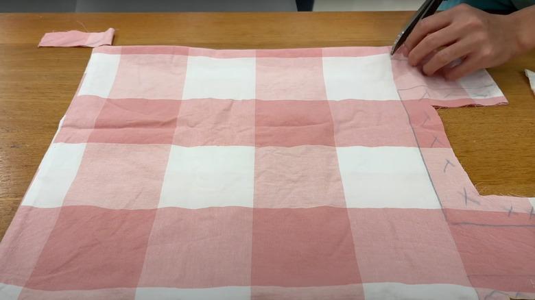 piece of fabric marked with lines, being cut by person on a tabletop