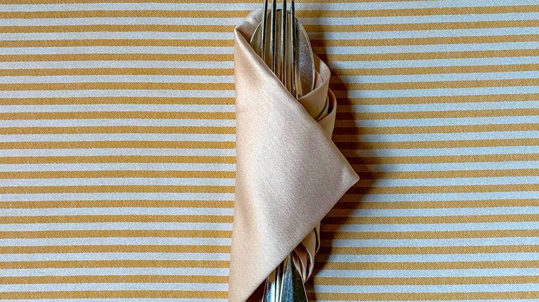 satin taupe fabric wrapped around silver utensils on striped surface