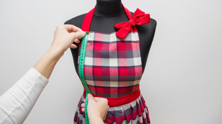 person measuring apron on sewing mannequin with measuring tape