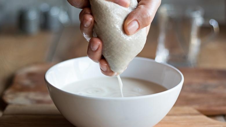 person straining with cheesecloth into white bowl