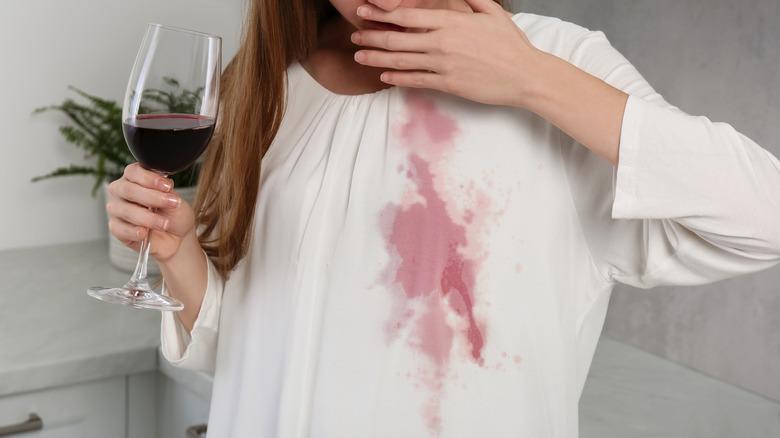 Woman with red wine in glass and spill on white shirt