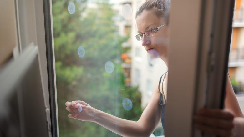 A woman putting many bird decals on a sliding glass door.
