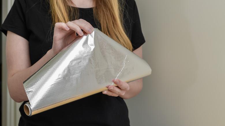 person unrolling aluminum foil from box