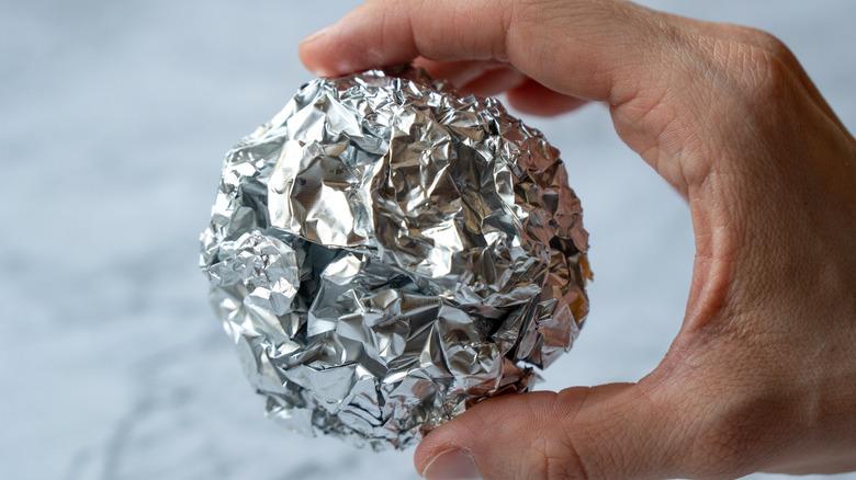 person holding aluminum foil ball between their fingers