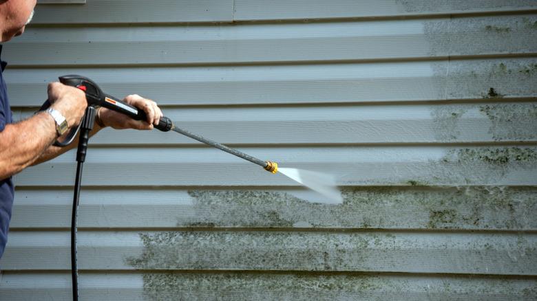 man pressure washing vinyl siding