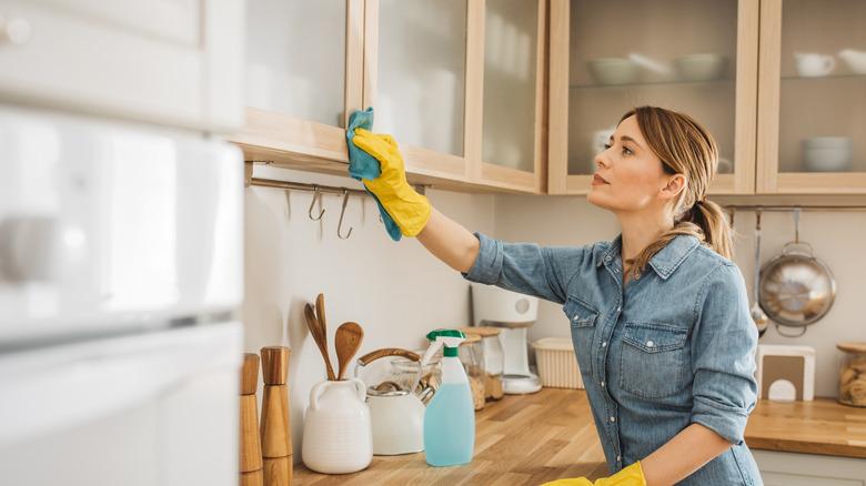 woman wiping glass-front wooden cabinet boxes with a cloth
