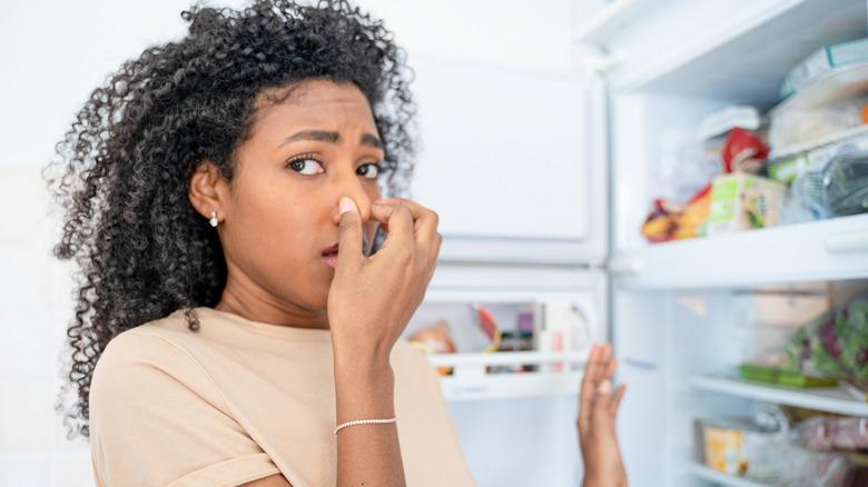 woman plugging her nose while opening the fridge in a kitchen