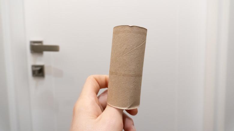 person holding a toilet paper tube in front of a door