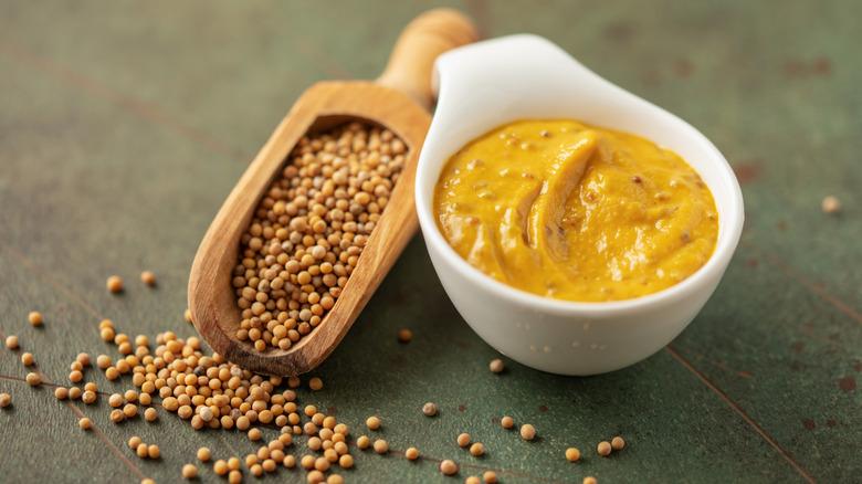 Mustard seeds in a scoop next to small dish of mustard