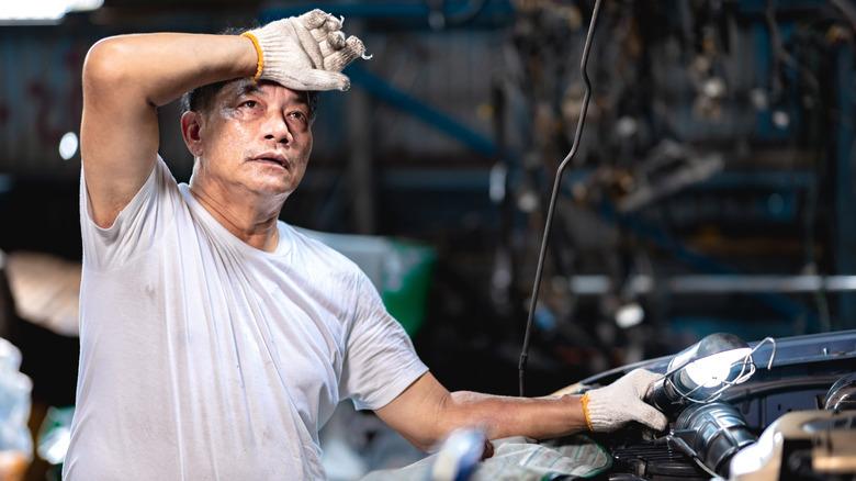 man sweating while working on car in garage