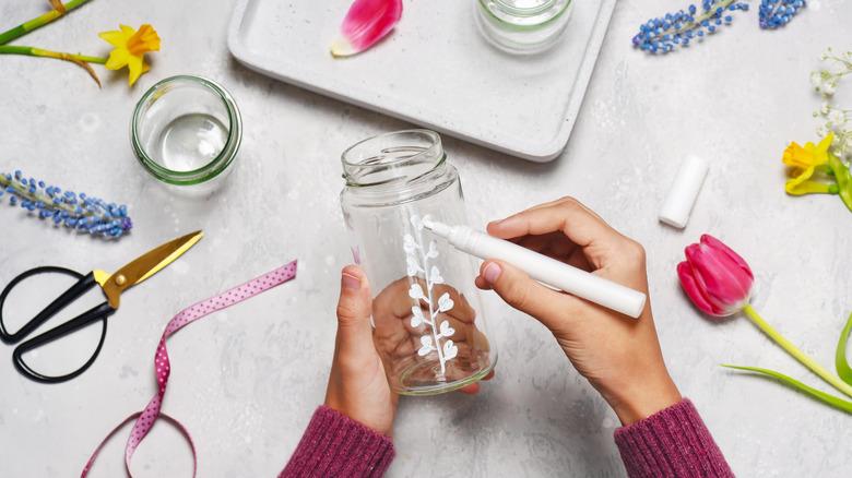 Person drawing flowers on glass jar with white marker