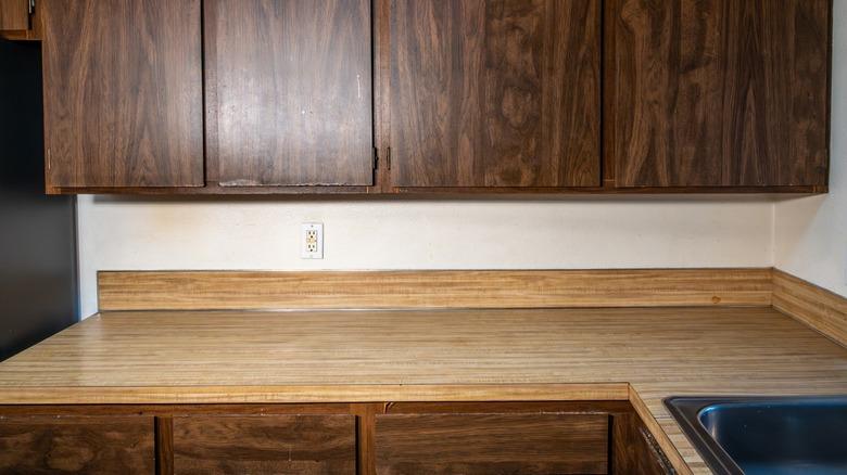 Interior view of a dated laminate kitchen counter and dated wood laminate cabinets.
