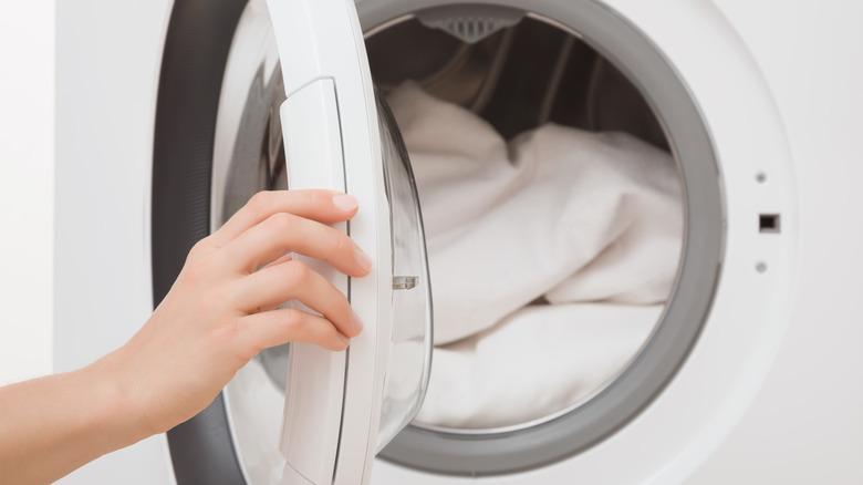 A dryer loaded with white sheets and hand on dryer door