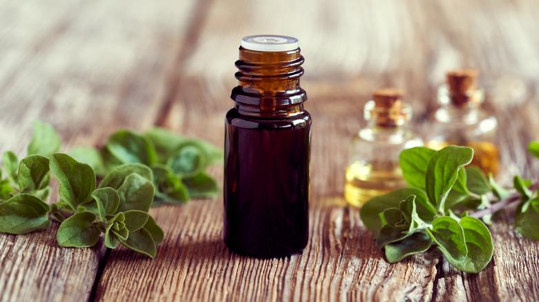 A dark bottle of essential oil with fresh marjoram twigs on a wooden table.