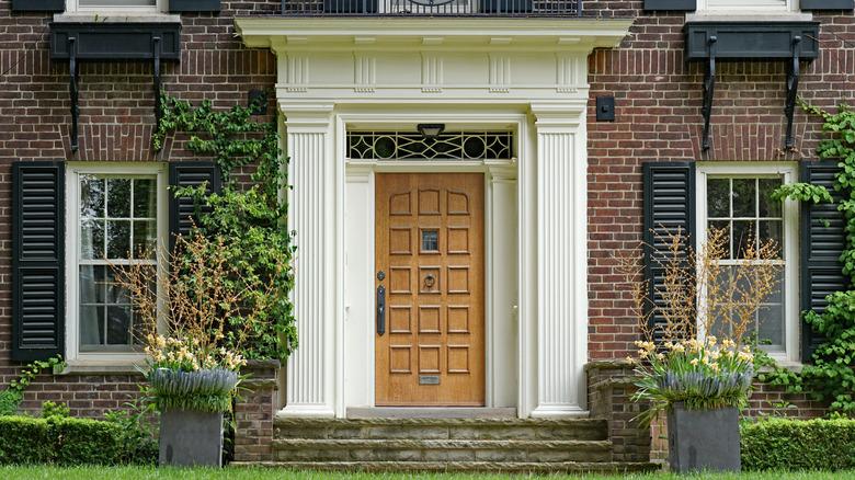 A blonde wooden door with black shutters on a brick home.