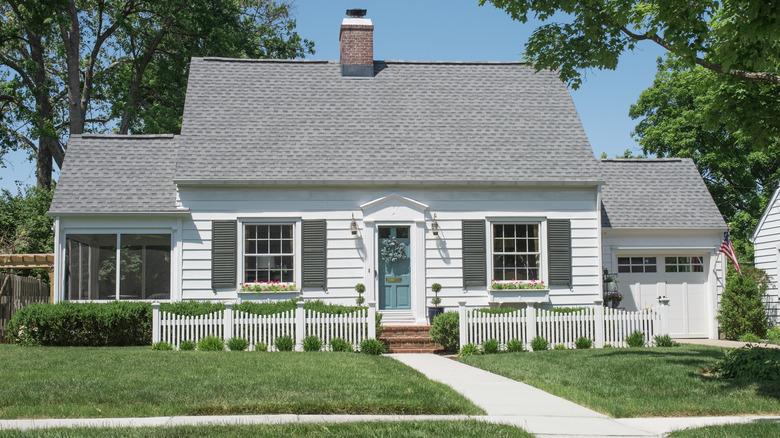 A Cape Cod style home with a blue door and gray shutters with a gray roof.