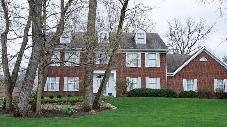 A stately brick home with white shutters and a white front door with a green front lawn.