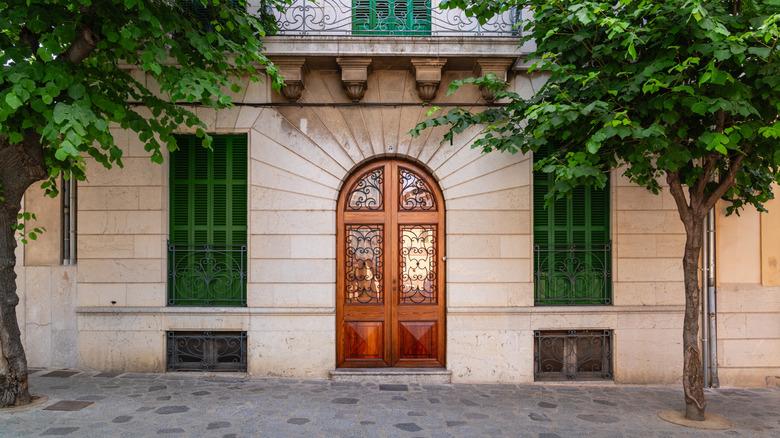 A rounded wooden door with green shutters on a European-style building.