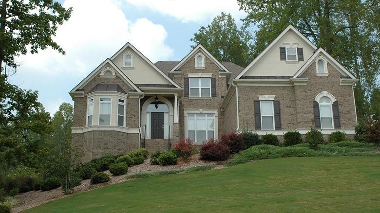 A brick house on a hill with gray shutters and front door.