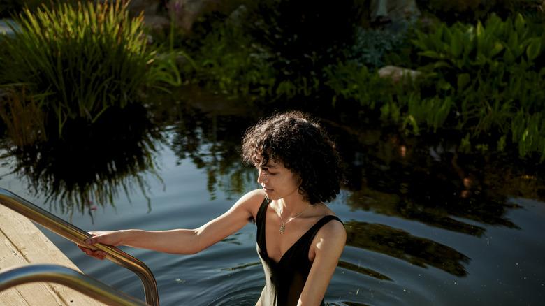 woman stepping onto a ladder out of a natural pool surrounded by grasses
