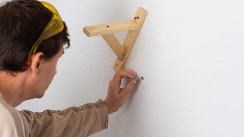 Man installing plastic anchor next to wooden shelf