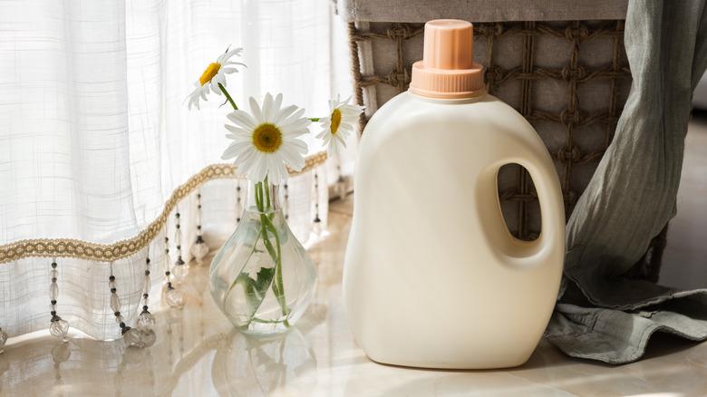 bottle of laundry detergent on table next to vase of flowers and full laundry basket