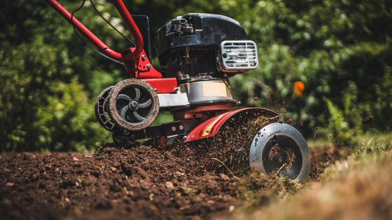 Close-up photo of a gardener cultivating soil with a rototiller