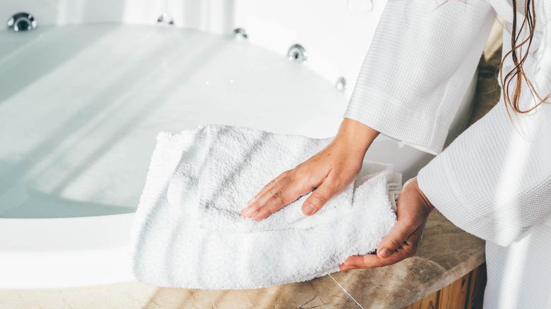 Woman placing white towels on edge of bath tub.