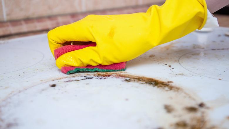 gloved hand cleaning dirty stovetop