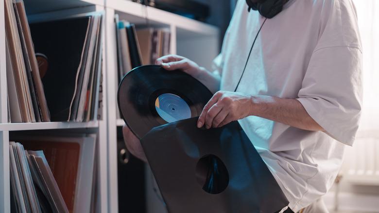 person putting a vinyl LP back into the sleeve in front of cube storage full of records