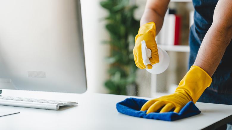 A gloved hand holds a spray bottle of disinfectant