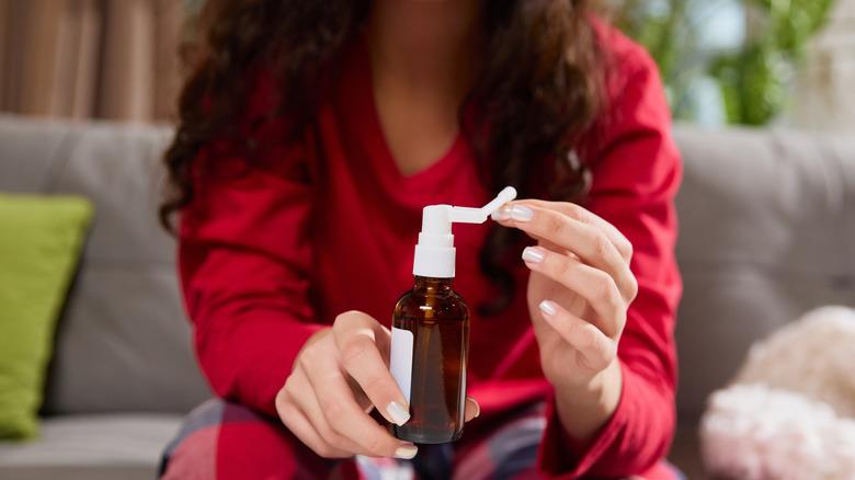 A person adjusts the spray nozzle on brown glass bottle, sitting on couch in living room.