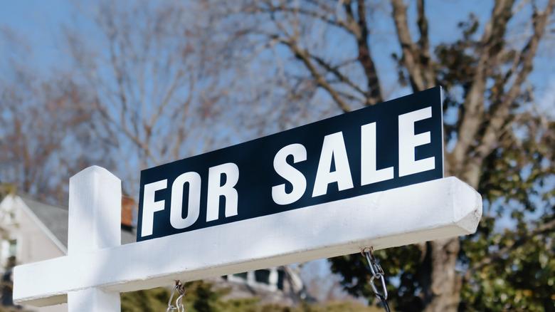 black and white "for sale" sign outside of a home on white post