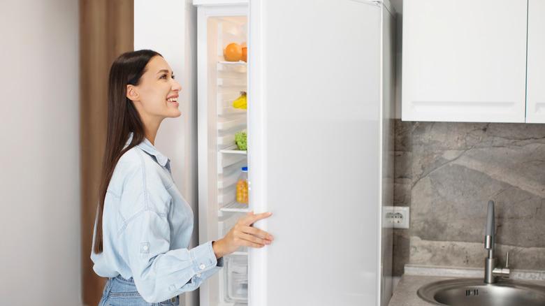 smiling woman looking into white refrigerator