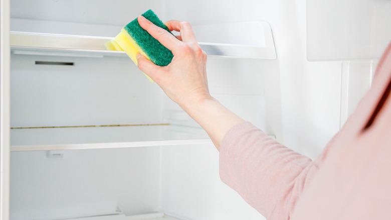 Woman wiping a fridge shelf with a sponge