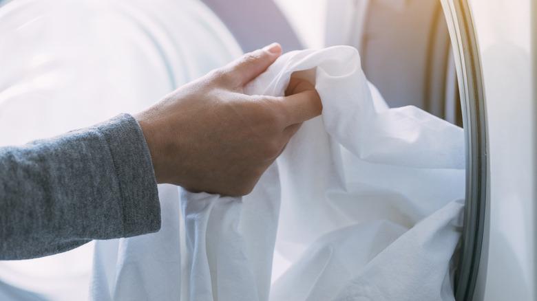 hand putting a white bedsheet into the laundry machine
