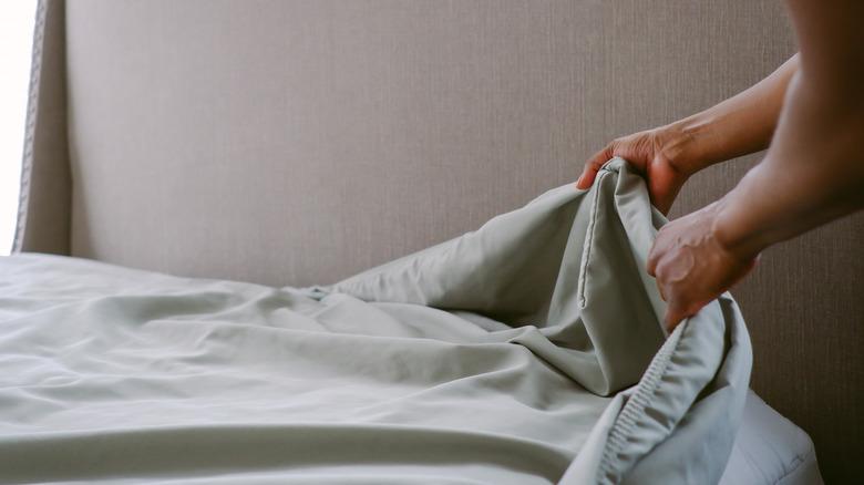 person changing sage green sheets