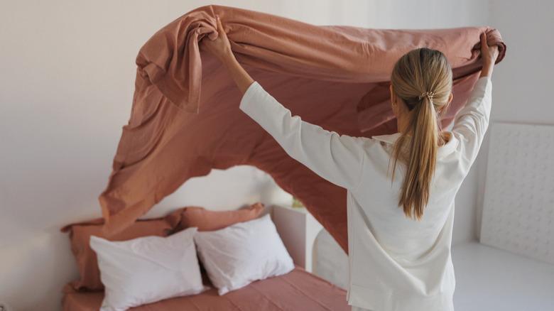 Woman fluffing clean comforter before laying on bed