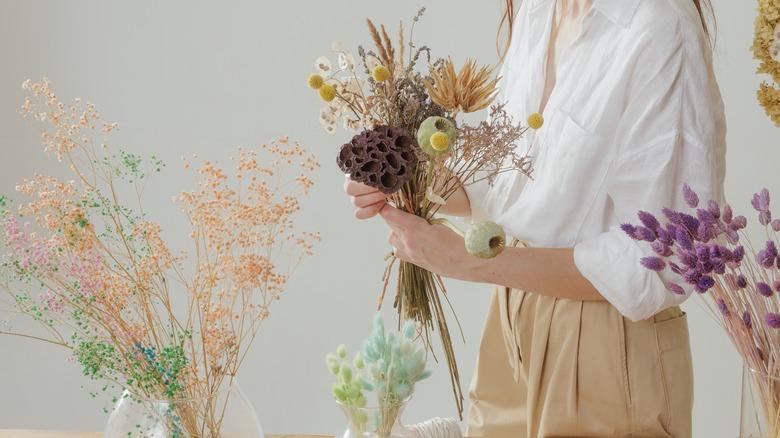 A woman with a bundle of dried flowers in her hand and various dried flower bundles on the table.